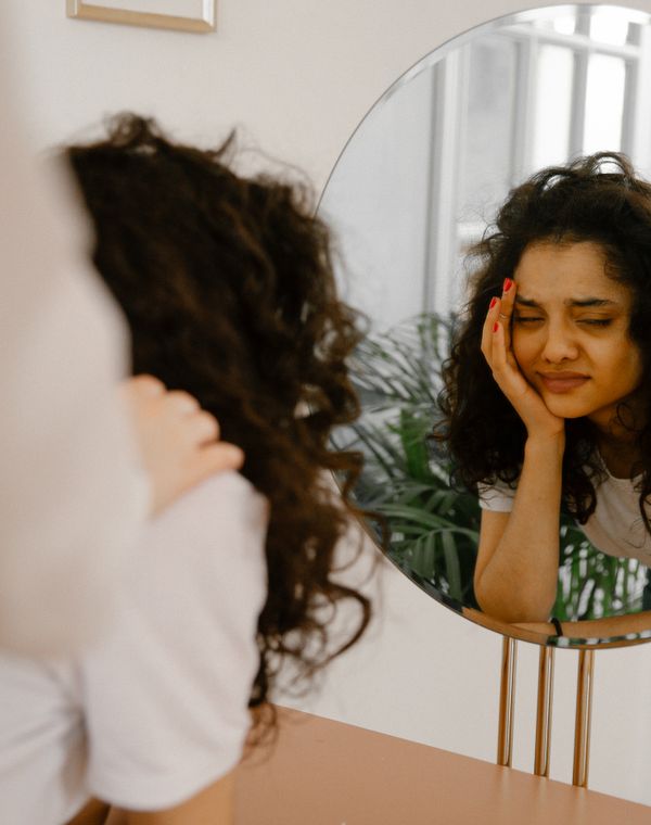 A woman at a mirror, head in her hand