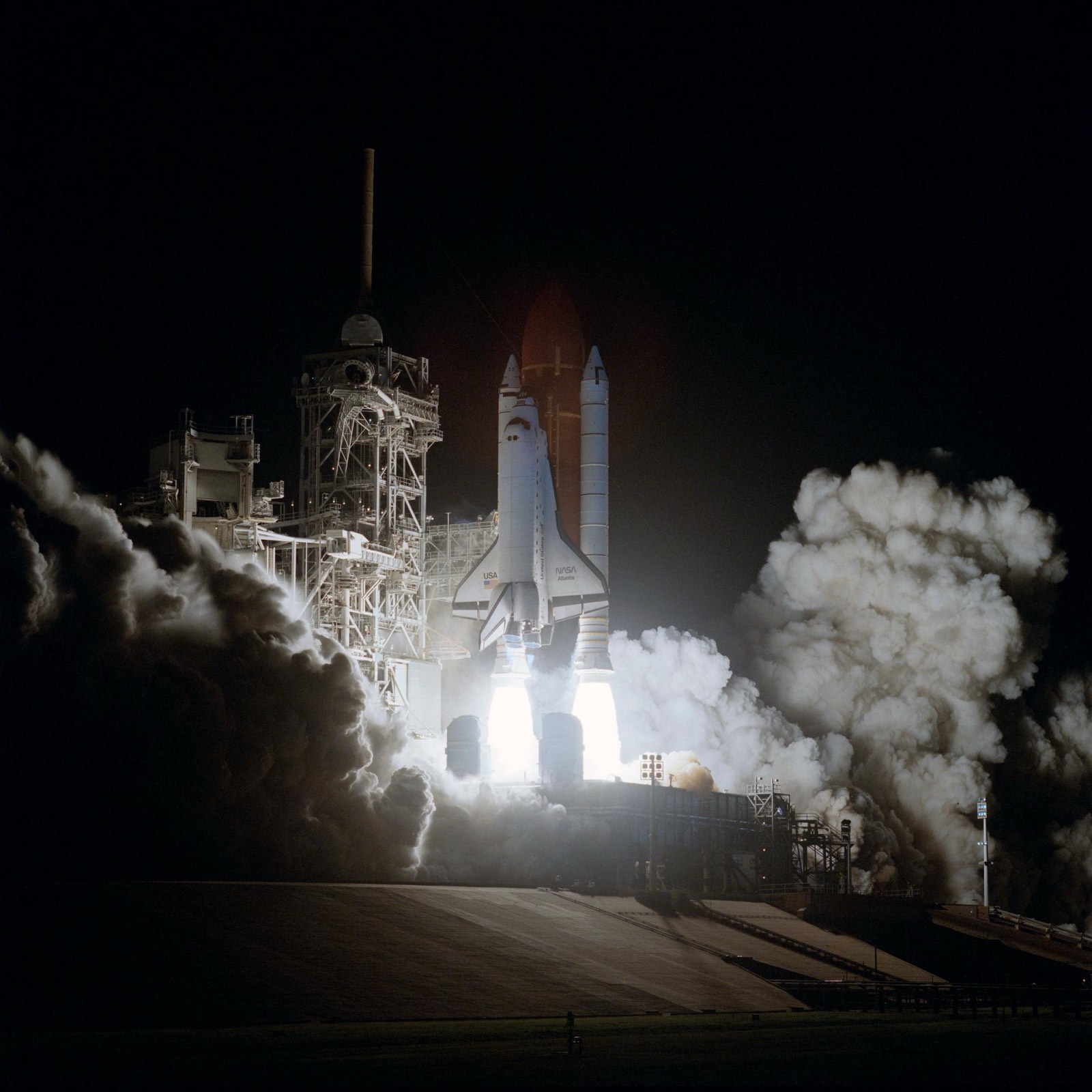Space shuttle Atlantis igniting on the launch pad at night, floodlit through the smoke